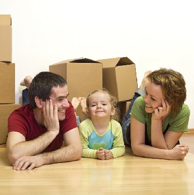 Happy couple with a kid in their new home laying on the floor with cardboard boxes around